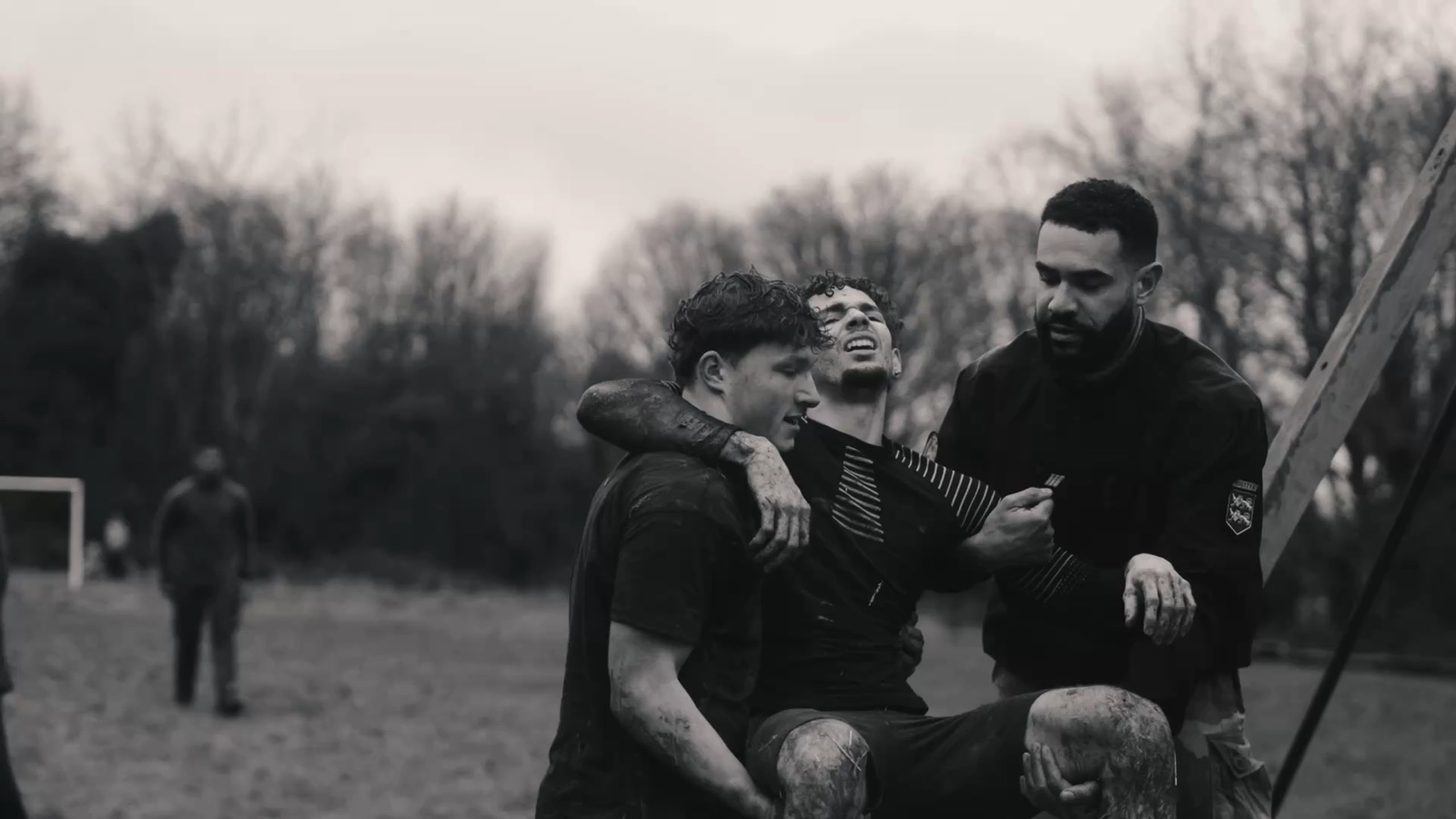 Muddy athletes carrying an exhausted teammate — black-and-white still from the BDE STAPS aftermovie
